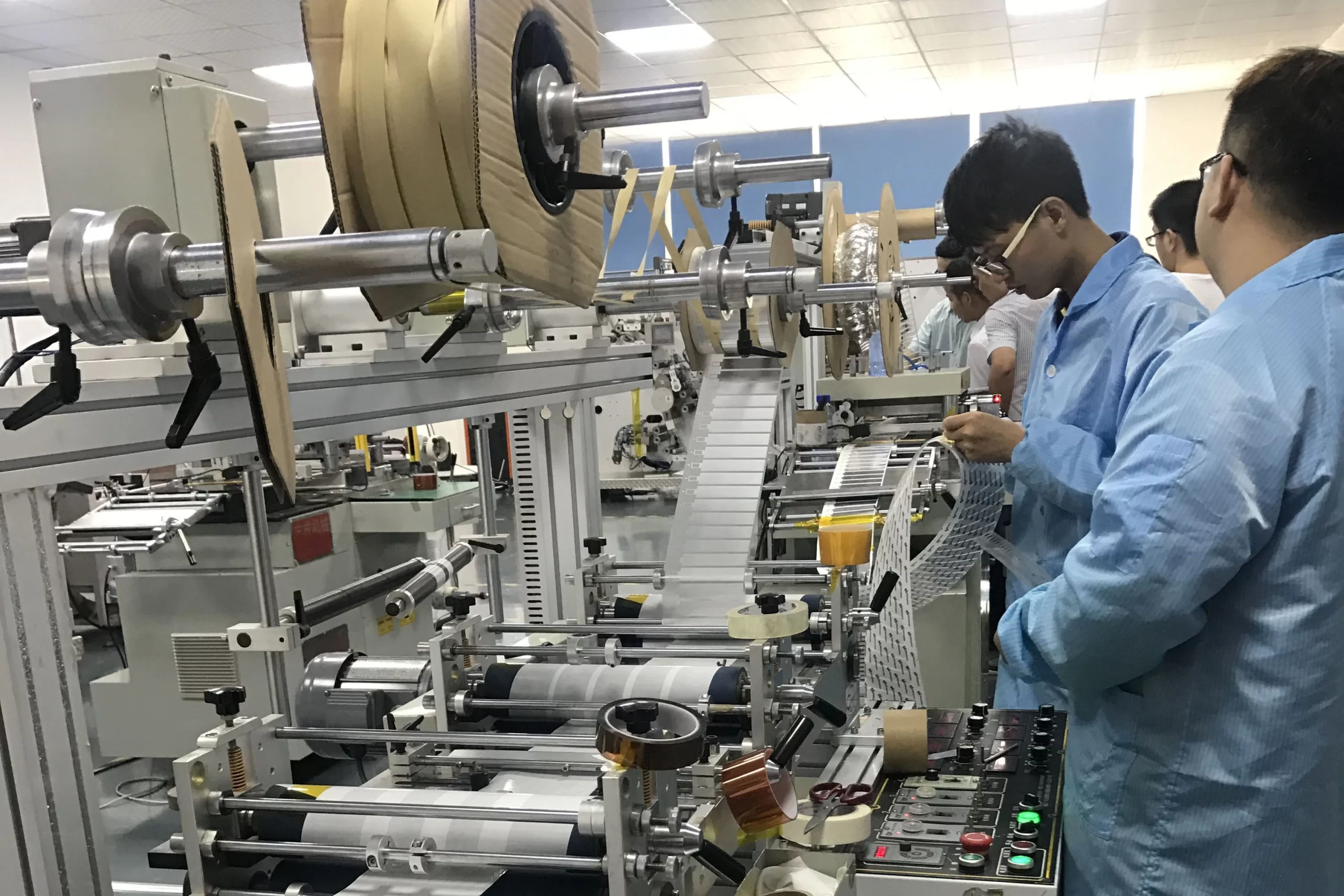 Due tecnici in camice blu azionano e ispezionano macchinari automatizzati in un moderno impianto di produzione.